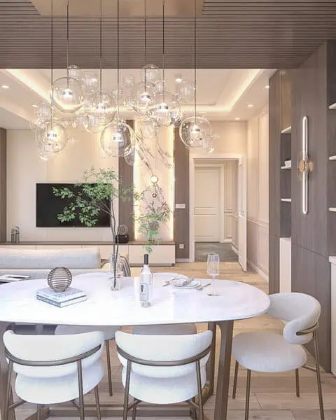 Küçükyalı salon tasarımı içinde mermer görünümlü yemek masası, cam avize, ahşap kitaplık ve aydınlatmalı raflar